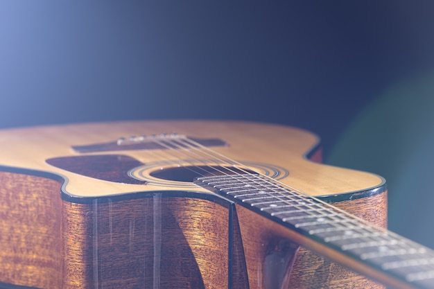 Guitarra acústica com uma bela madeira em um fundo preto à luz de um holofote.