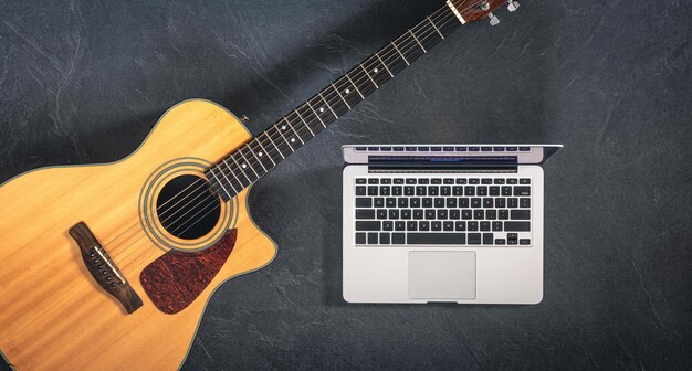 Guitarra acústica e laptop em um fundo preto texturizado vista superior