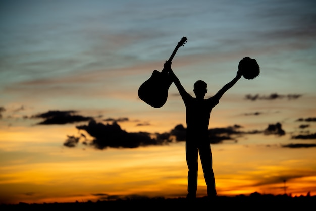 Guitarrista de garota de silhueta em um pôr do sol