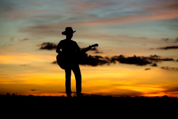 Guitarrista de garota de silhueta em um pôr do sol