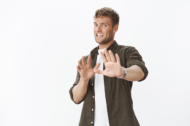 Foto grátis guy rindo nervosamente e inclinando-se para trás com um sorriso estranho e preocupado, estendendo as mãos em defesa, tentando acalmar o companheiro indignado, dizendo espere, pare ou relaxe sobre a parede cinza