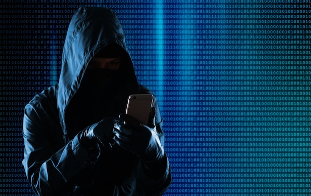 Hacker de crime cibernético encapuzado usando internet do telefone móvel invadindo o ciberespaço, o conceito de segurança de dados pessoais online.