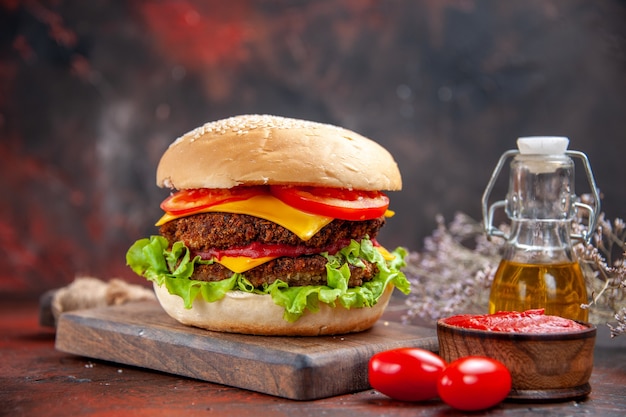 Hambúrguer de carne de frente com tomate, queijo e salada em fundo escuro