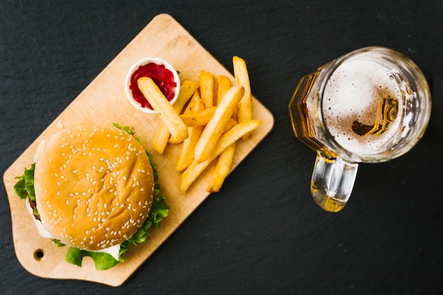 Hamburguer e batatas fritas na placa de madeira com cerveja