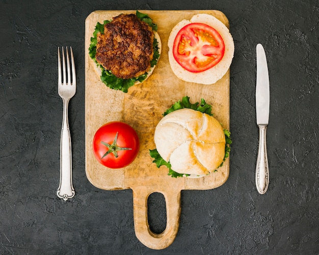 Foto grátis hamburguer flat-lay na placa de madeira com talheres