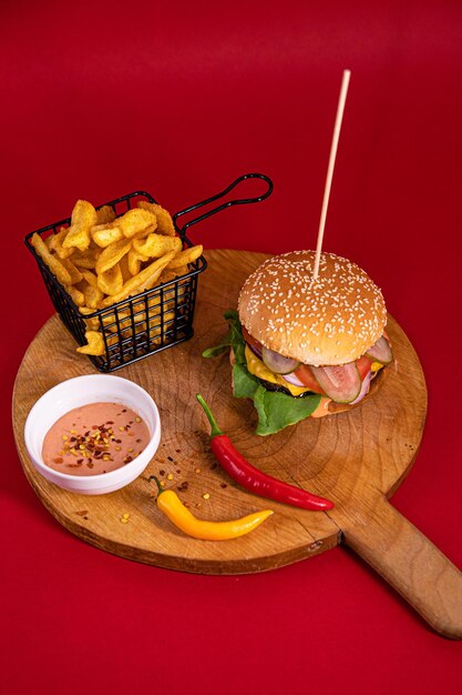 Hambúrguer grande, batatas fritas, molho Fry e duas pimentas servidos em uma tábua de madeira