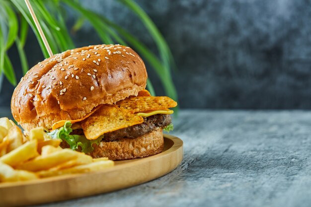 Hambúrguer grande com batata frita no prato de madeira na superfície de mármore