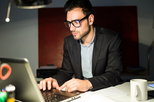 Handsome jovem empresário trabalhando com laptop no escritório.