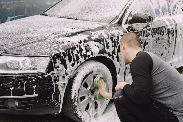 Handsomen homem em um suéter preto lavando seu carro