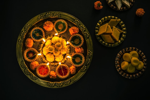 Happy diwali - flower rangoli com doces ou mithai e diya em tigelas para o diwali ou qualquer outro festival na índia, foco seletivo