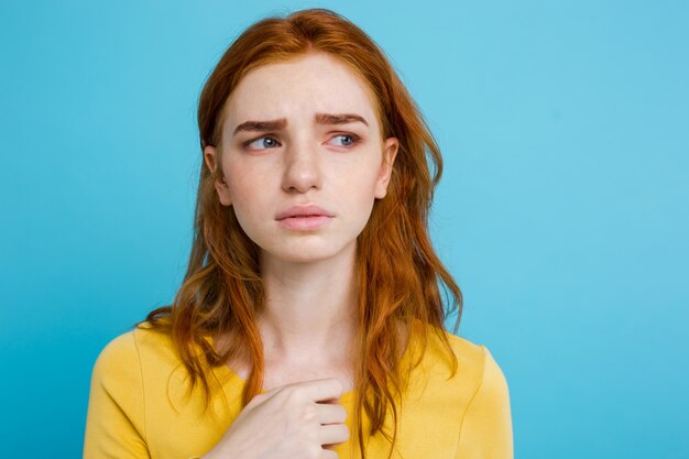 Headshot Retrato de adolescente redhead tênue com expressão séria olhando para a câmera. Modelo de mulher caucasiana com cabelo de gengibre posando em ambientes internos.Pastel background azul. Espaço de cópia.