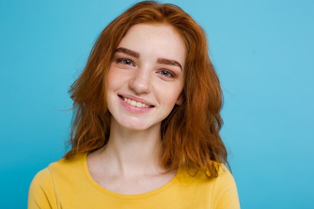 Headshot Retrato de feliz gengibre menina de cabelo vermelho com sardas sorrindo olhando câmera. Fundo azul Pastel. Espaço de cópia.