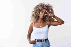 Foto grátis hipster à moda jovem afro-americana blogueira de beleza loira penteado encaracolado sorrindo encantado segurar mão jeans mostrar vitória paz gesto perto de inclinação do olho cabeça expressar alegremente atitude positiva