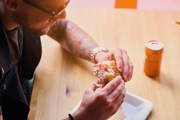 Hipster atraente vestido com jaqueta de couro comendo um hambúrguer vegano.