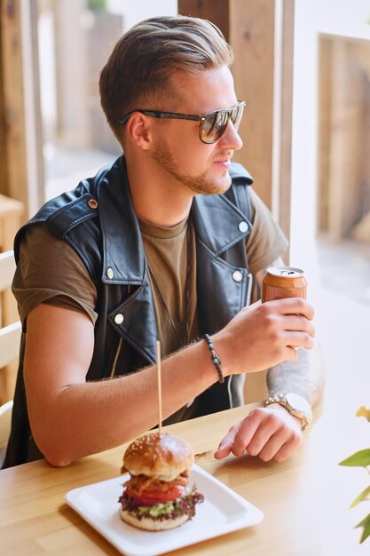 Hipster atraente vestido com jaqueta de couro comendo um hambúrguer vegano.