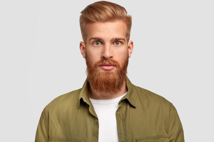 Foto grátis hipster bonito tem barba ruiva, penteado moderno, olha sério diretamente para a câmera, contempla sobre um futuro emprego