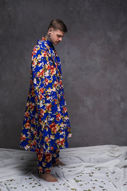 Foto grátis hipster jovem em floral longo drape olhando folhas caindo em pano branco contra parede cinza