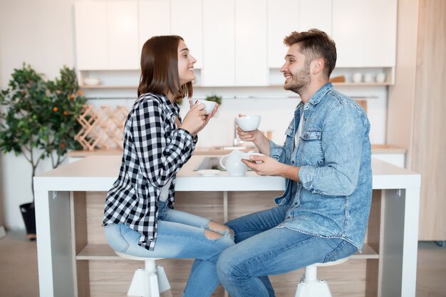 Hipster legal jovem feliz e mulher na cozinha, café da manhã, casal pela manhã, sorrindo, tomando chá