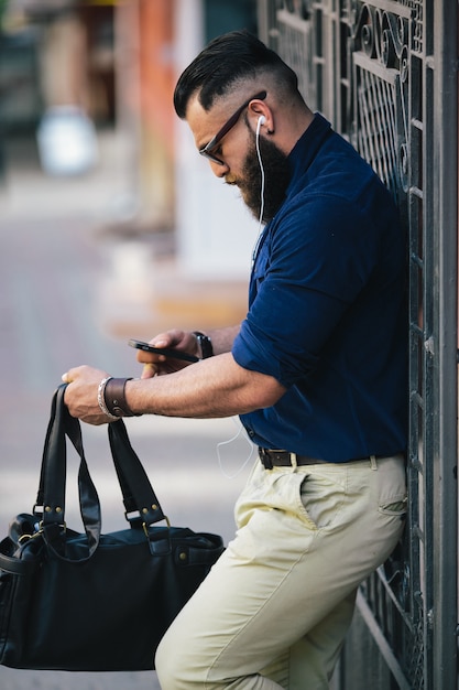 Homem à moda segurando sua bolsa e usando o seu celular