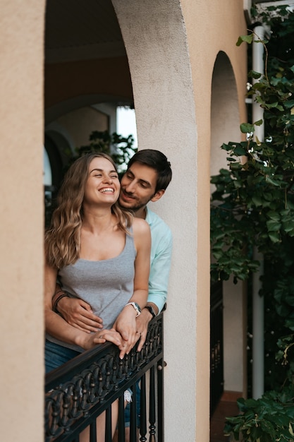 Foto grátis homem abraçando a esposa na varanda. casal relaxado aproveita o dia e boas notícias. jovem familia feliz