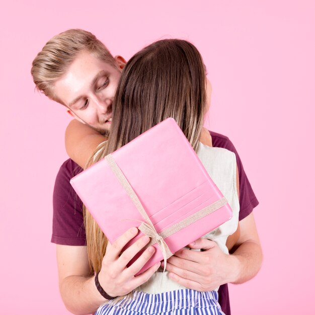 Homem, abraçando, dela, namorada, segurando, caixa presente, contra, cor-de-rosa, fundo