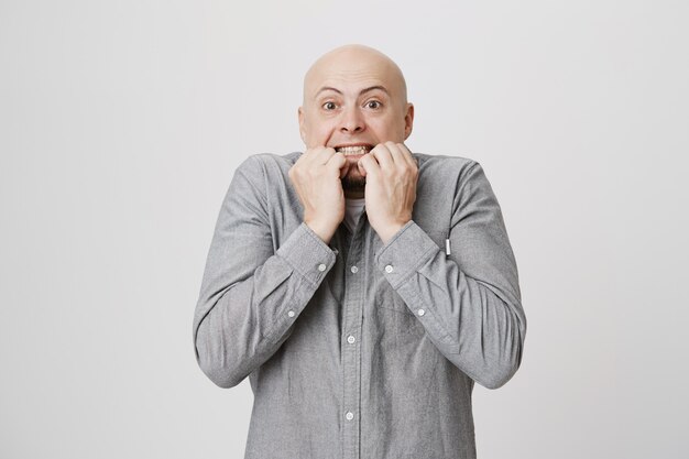 Homem adulto careca preocupado roendo as unhas