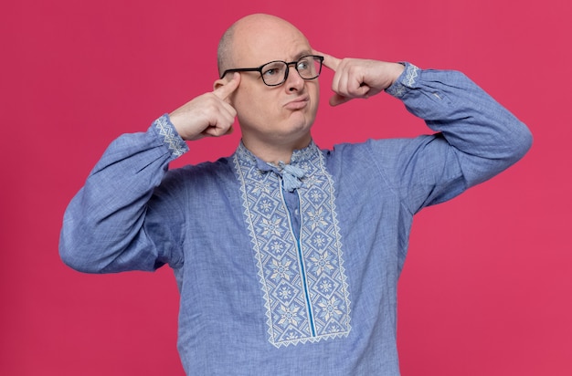 Homem adulto confuso com camisa azul e óculos, colocando os dedos nas têmporas e olhando para o lado