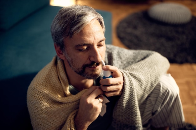 Foto grátis homem adulto médio envolto em um cobertor usando spray nasal em casa