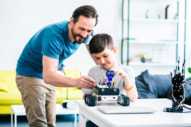Homem adulto positivo ajudando seu filho com engenharia robótica enquanto testa sua criação