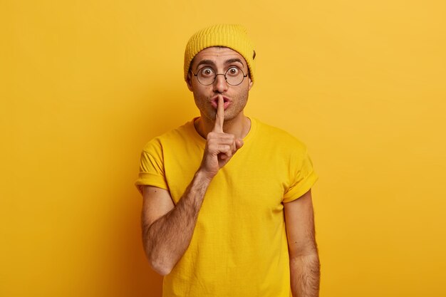 Homem adulto surpreso que guarda fofoca, fica quieto e calado, com o dedo indicador sobre a boca, conta segredos