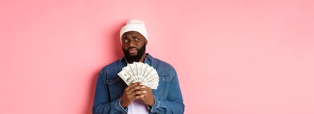 Foto grátis homem africano-americano hesitante segurando dinheiro olhando para a esquerda com dúvidas e preocupações contra pi
