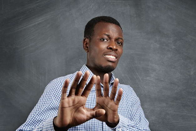 Foto grátis homem africano com expressão assustada no rosto, fazendo um gesto assustado com as palmas das mãos, como se estivesse tentando se defender de alguém. temível homem de pele escura pedindo para parar, gesticulando com as mãos