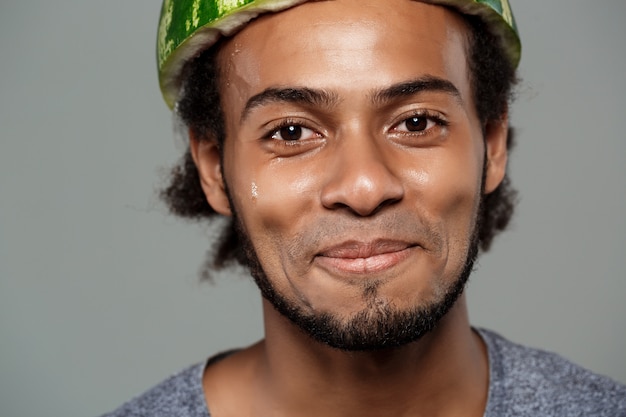 Homem africano com melancia na cabeça, enganando a parede cinza.