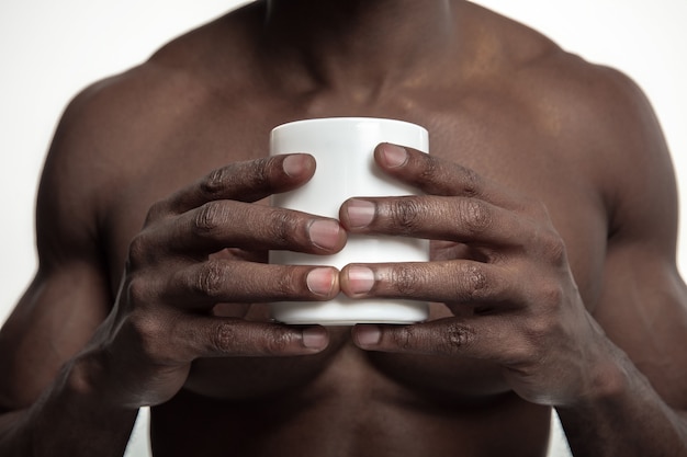 Homem africano com uma xícara branca de chá ou café, isolado no estúdio branco.