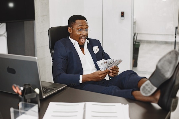 Foto grátis homem africano de terno preto. cara sentado à mesa. empresário com dinheiro.