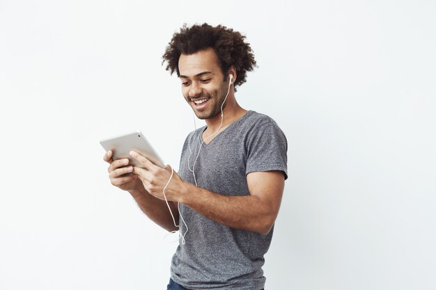 homem Africano em fones de ouvido rindo segurando tablet falando ou assistindo e desfrutando de um programa de comédia ou navegação.