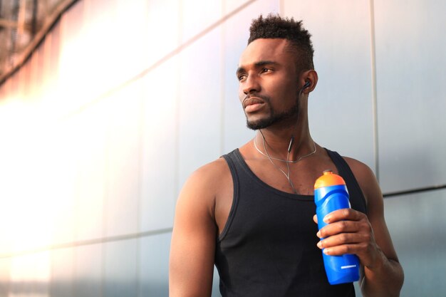 Homem africano em roupas esportivas, beber água enquanto está do lado de fora, ao pôr do sol ou nascer do sol. corredor.
