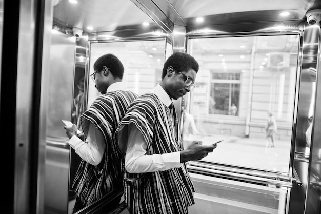 Foto grátis homem africano em roupas tradicionais e óculos com telefone celular em elavator ou elevador moderno