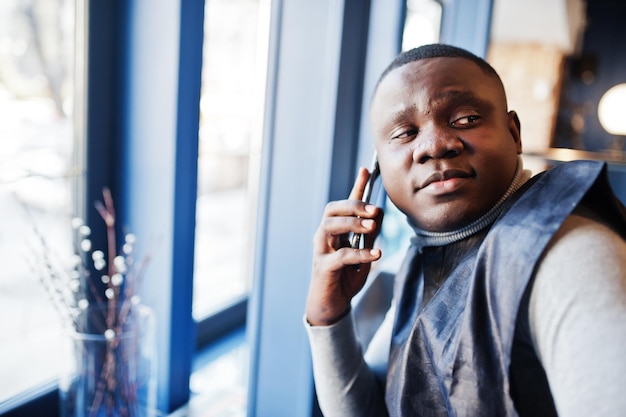 Homem africano em roupas tradicionais pretas, sentado no restaurante e falando no smartphone