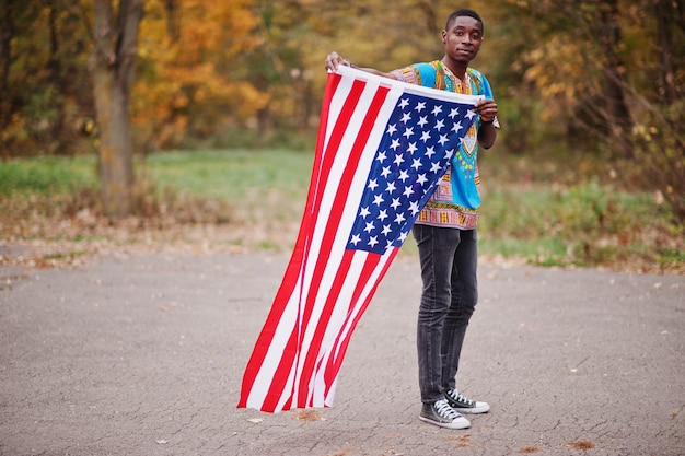 Homem africano na camisa tradicional da África no parque de outono com bandeira dos EUA