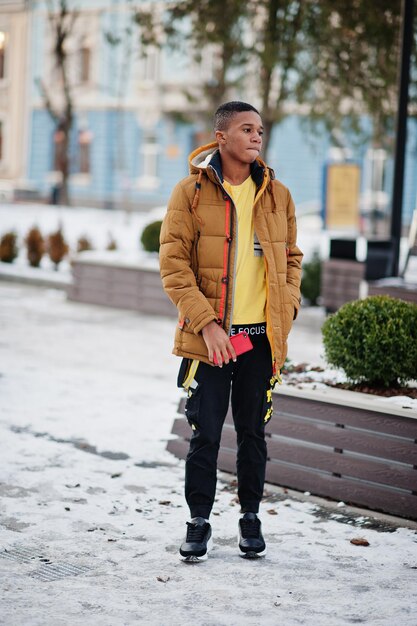 Homem africano usa jaqueta laranja no inverno frio posado ao ar livre com telefone celular