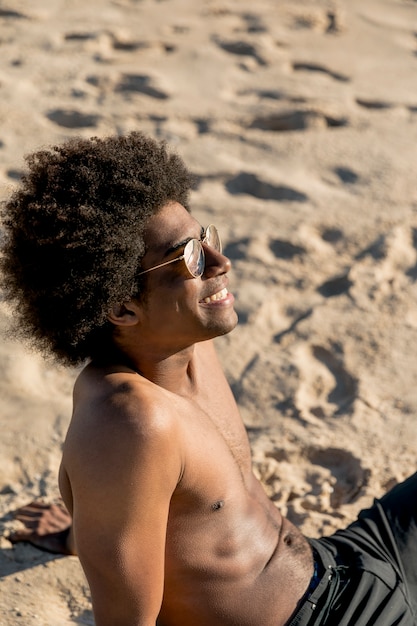 Homem afro-americano alegre sentado na areia na luz solar