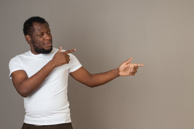 Homem afro-americano aponta para a esquerda com os dedos, em frente à parede cinza.