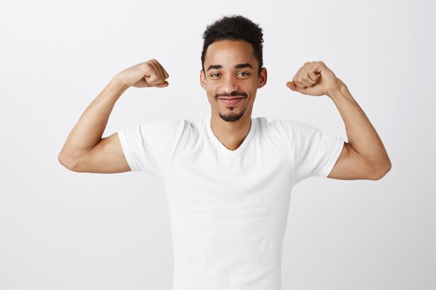 Homem afro-americano bonito, confiante e forte flexionando bíceps, malhando na academia, parecendo atrevido