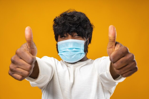 Homem afro-americano bonito positivo com máscara médica contra fundo amarelo