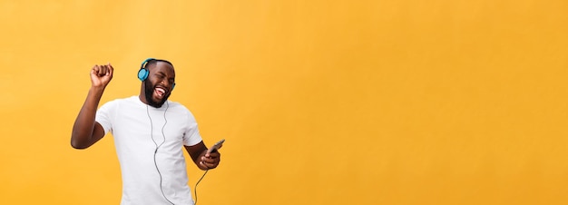 Homem afro-americano com fones de ouvido ouve e dança com música isolada em fundo amarelo