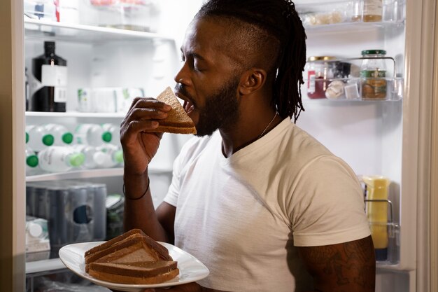 Homem afro-americano comendo na geladeira à noite