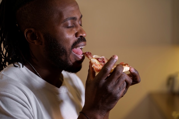 Homem afro-americano comendo pizza tarde da noite