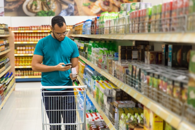 Homem afro-americano concentrado lendo a lista de compras em smartphone