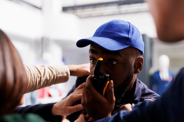 Homem afro-americano de segurança usando walkie-talkie enquanto segurava uma multidão de compradores. oficial de polícia gerenciando um grande grupo de pessoas na entrada da loja durante a temporada de compras de férias movimentada